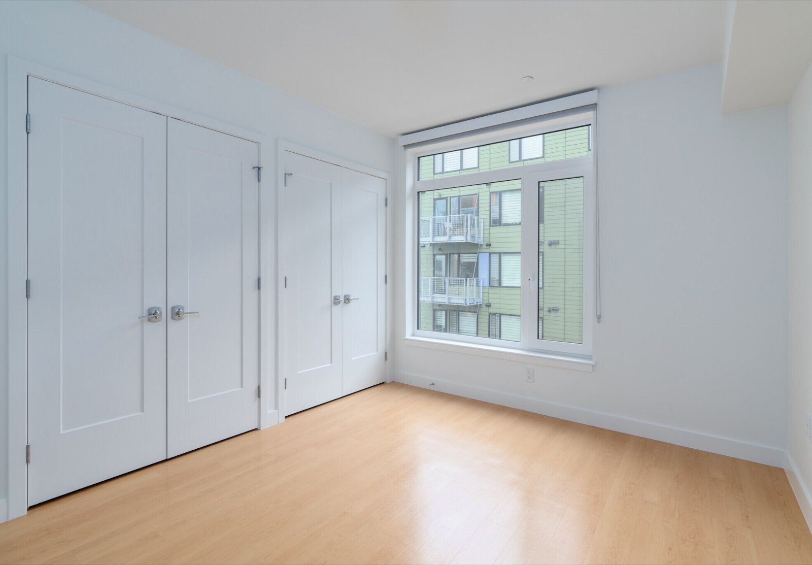 Empty bedroom, white walls, wood floor, closets, no people